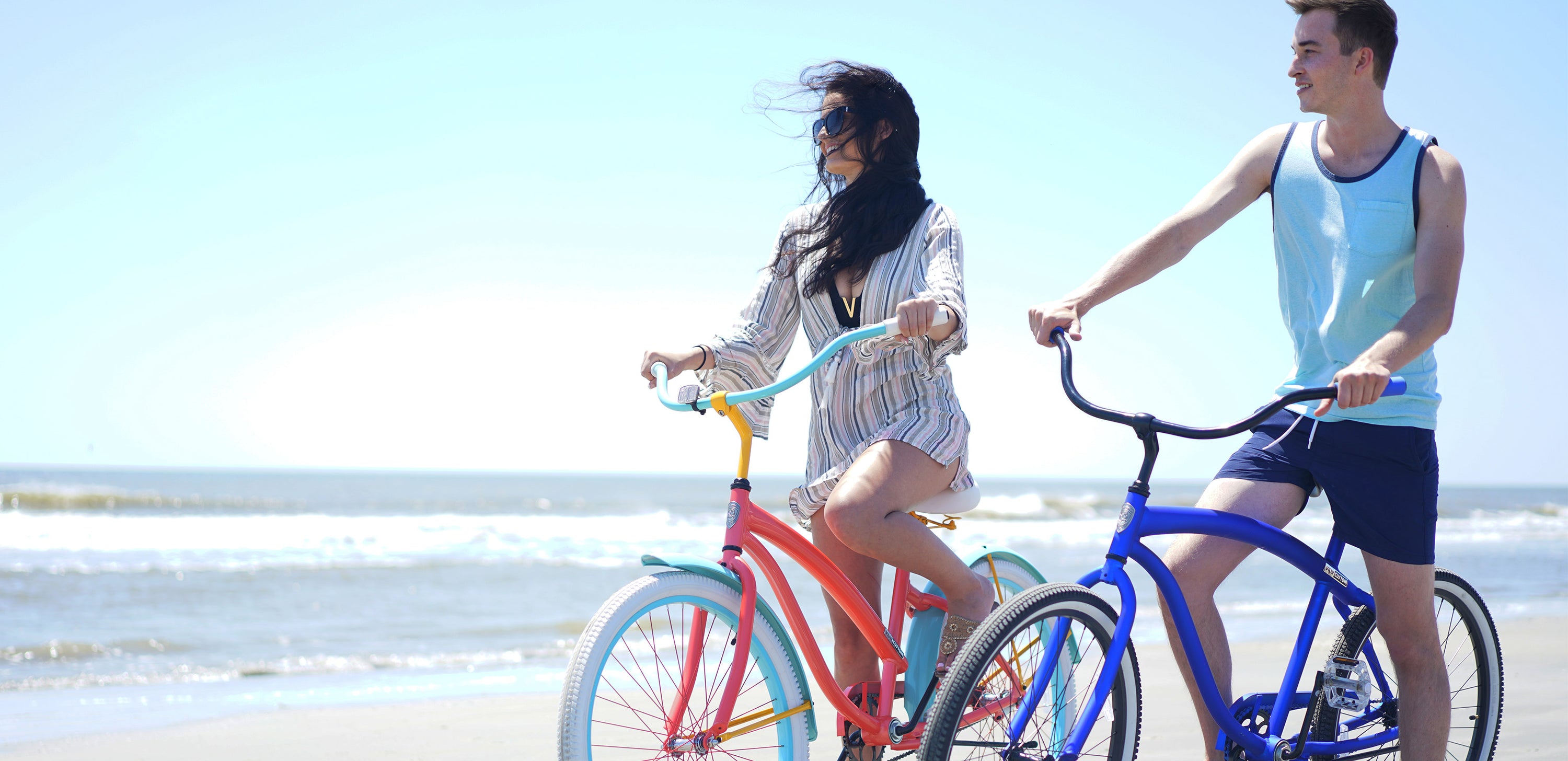 A girl on her pink Villy bike and a guy on his blue Villy bike enjoying the breeze on the beach shoreline
